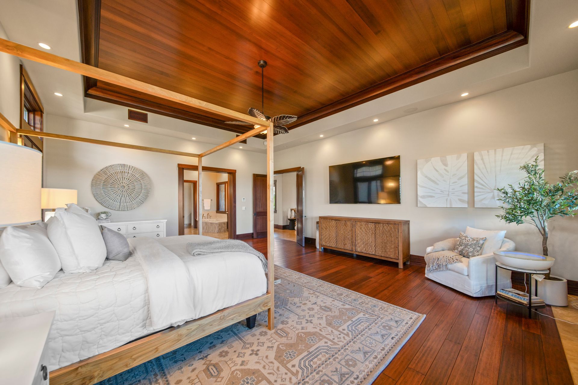 A large bedroom with a canopy bed , hardwood floors , a ceiling fan and a flat screen tv.