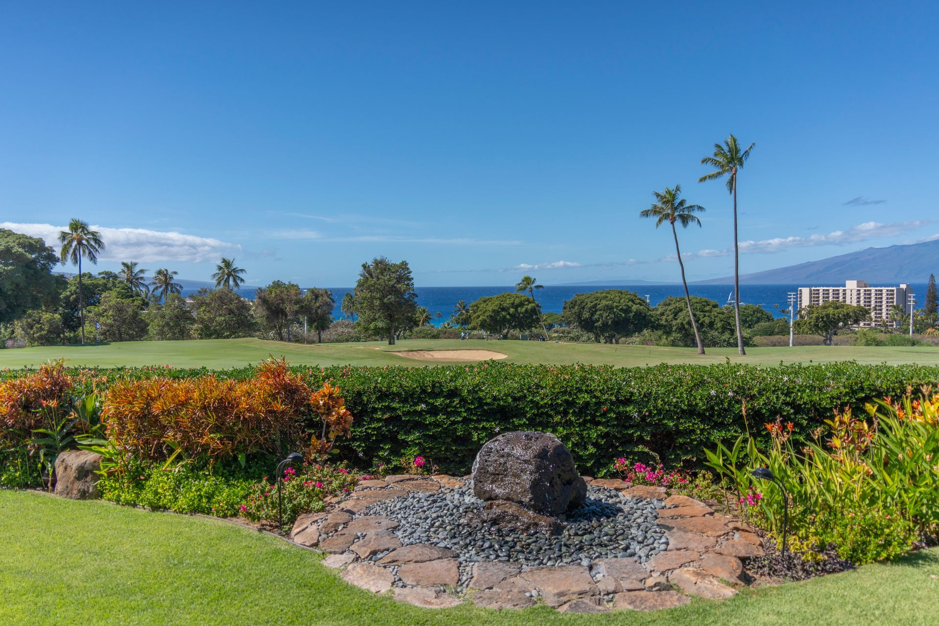 There is a fountain in the middle of the garden with a view of the ocean.