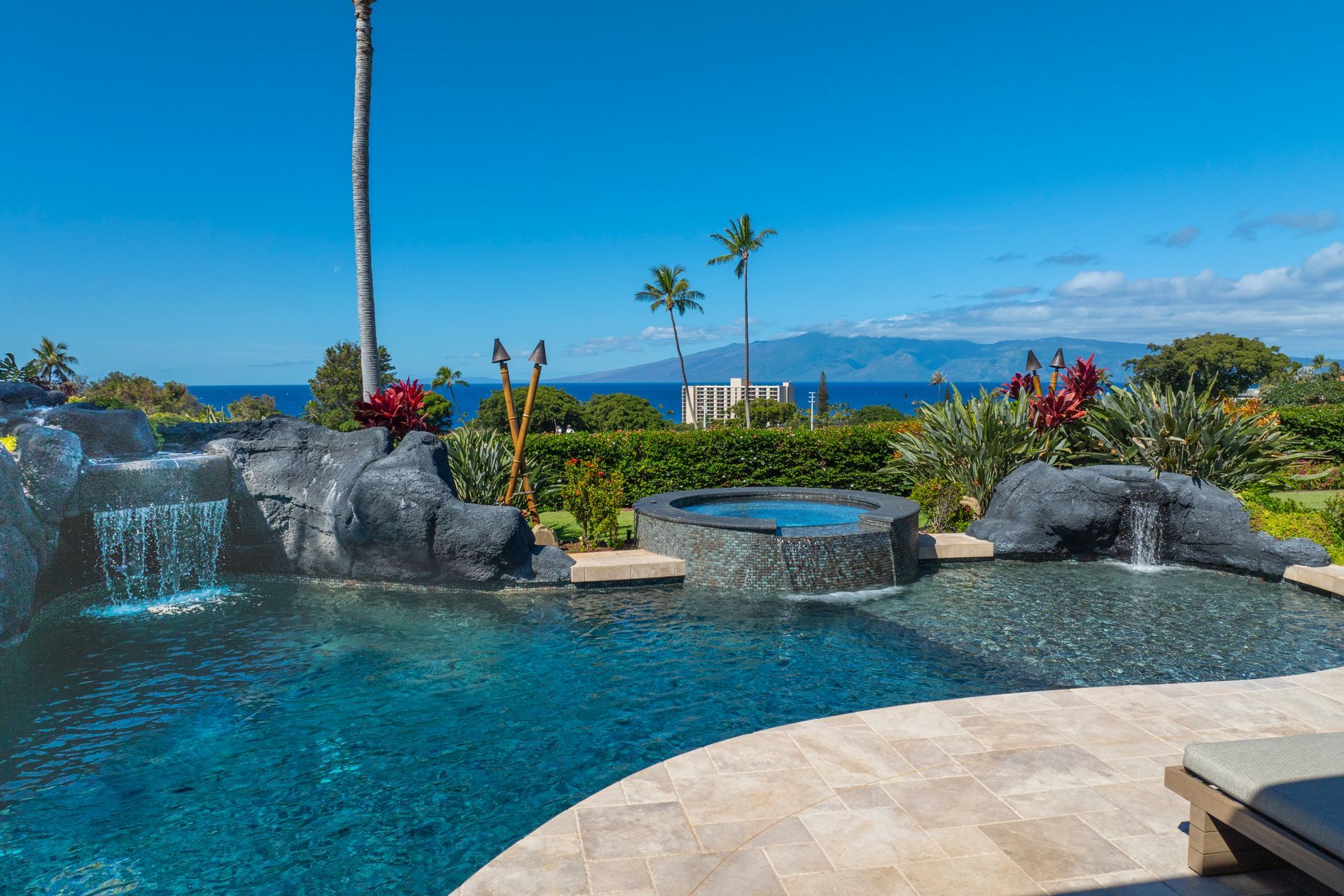 A large swimming pool with a waterfall and a view of the ocean.