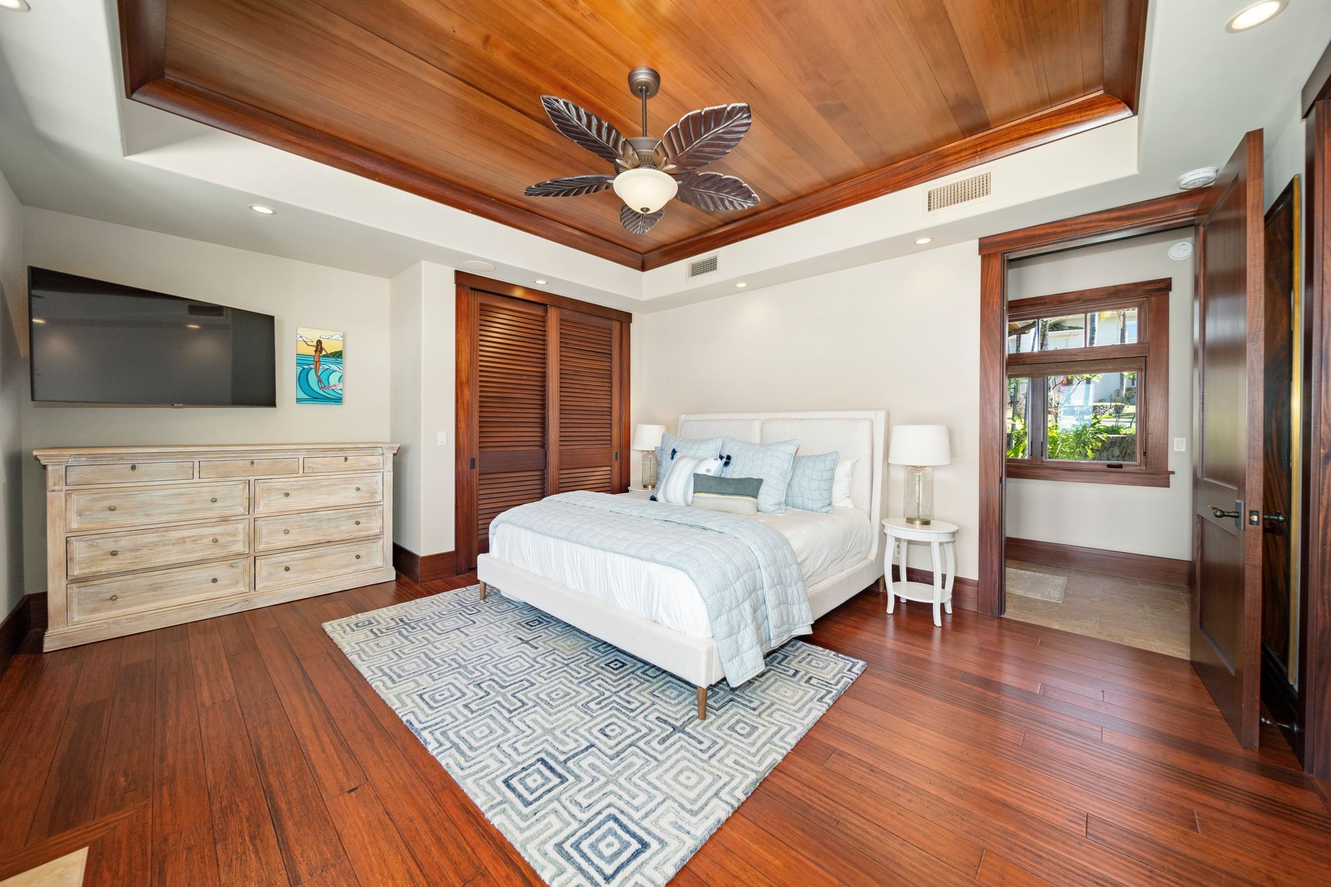 A bedroom with a bed , dresser , television and ceiling fan.