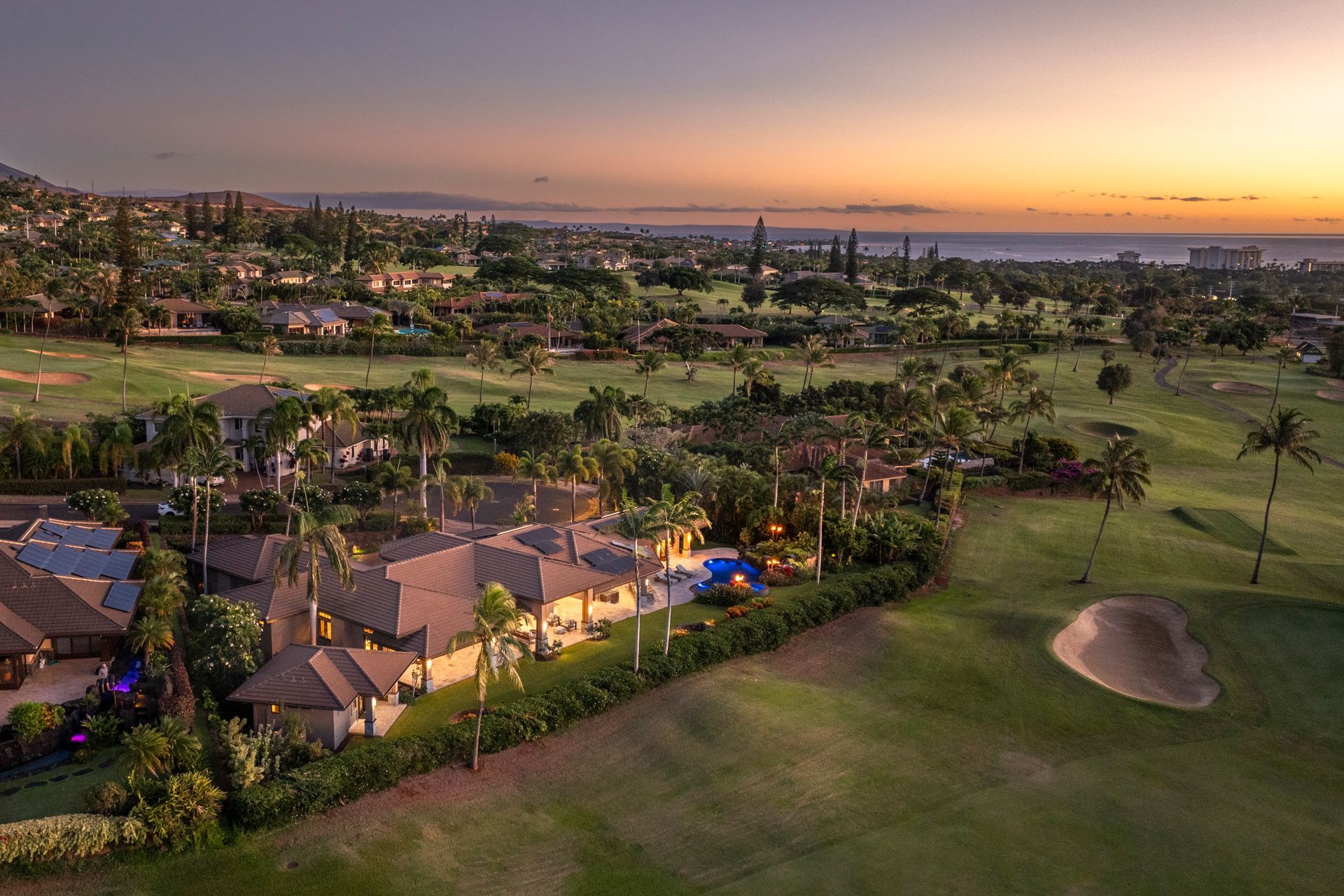 An aerial view of a golf course and houses at sunset