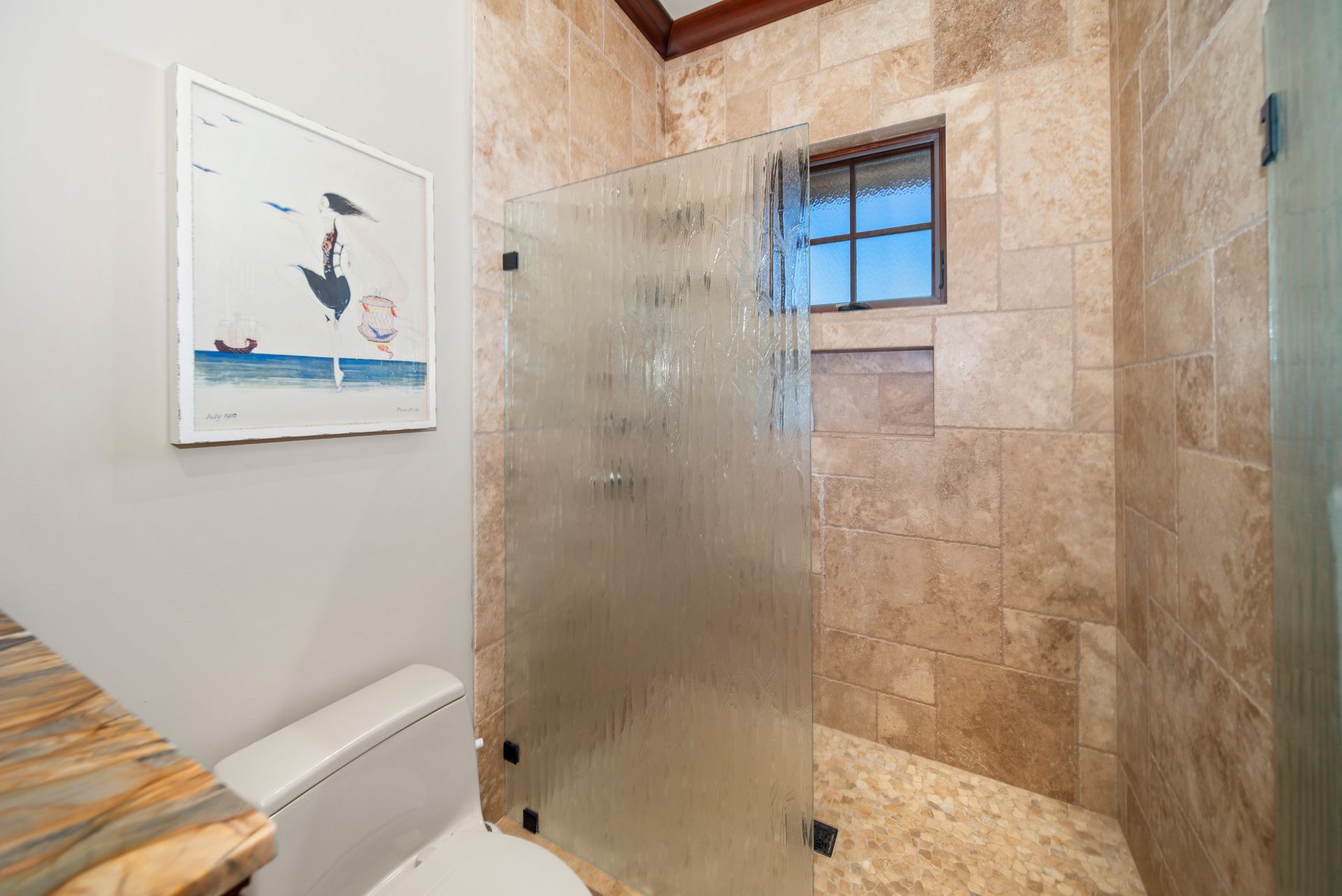 A bathroom with a toilet and a walk in shower with a glass door.