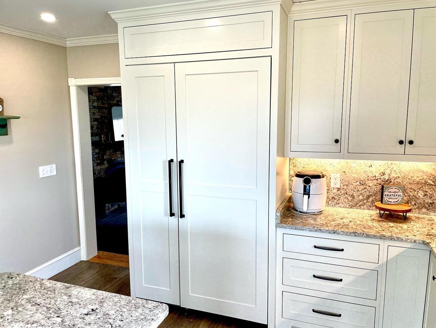 White kitchen cabinets with black handles; refrigerator and countertop with an air fryer.