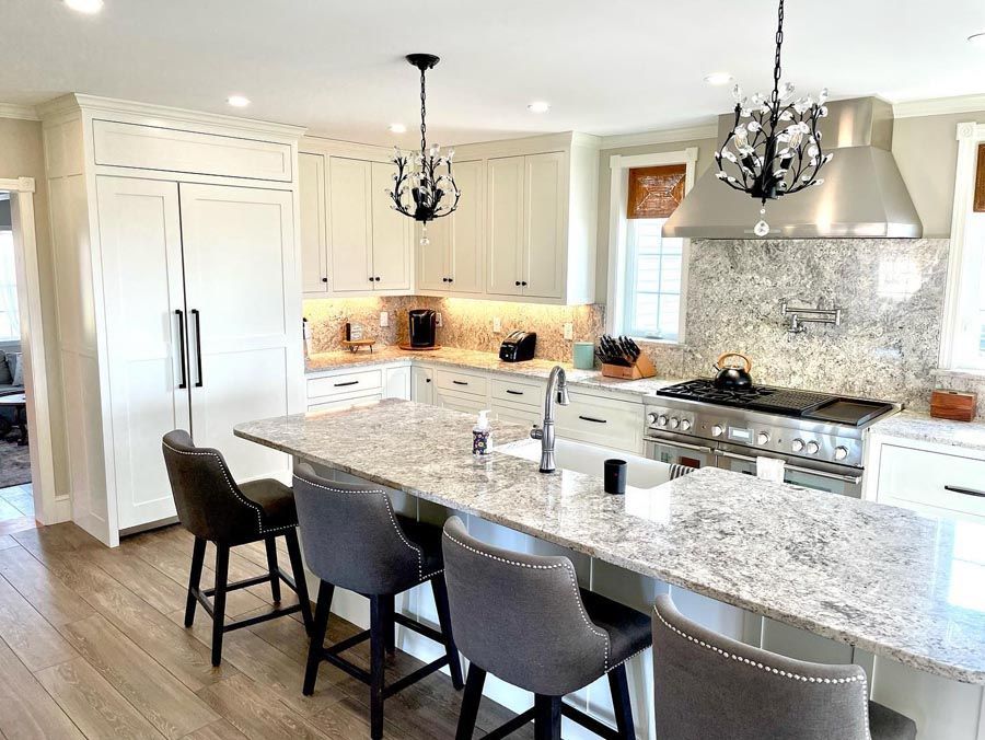White kitchen with granite countertops, stainless steel appliances, and two chandeliers.