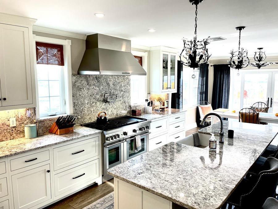 Spacious kitchen with white cabinets, granite countertops, stainless steel appliances, and black chandeliers.
