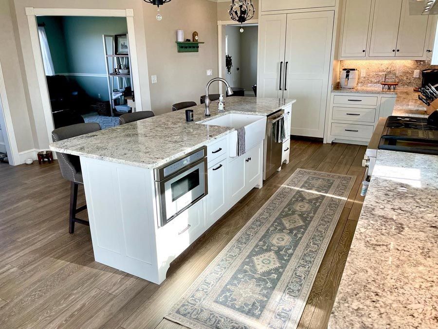 Kitchen with white cabinets, island with sink and microwave, rug, light wood floors, and granite countertops.