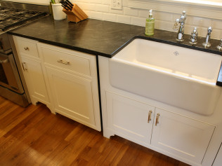 White kitchen cabinets with a farmhouse sink and black countertop.