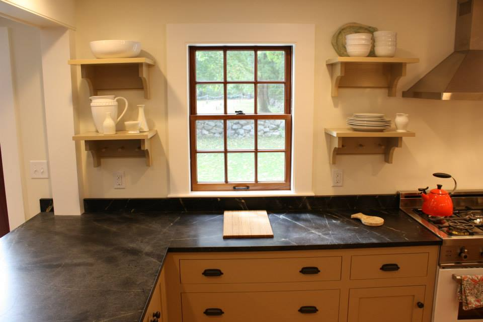 Kitchen with yellow cabinets, black countertops, shelves holding dishes, and a window.