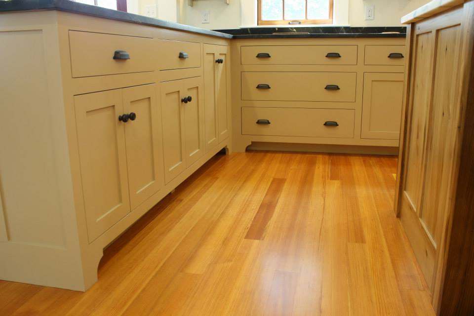 Cream-colored kitchen cabinets with black handles, set against a light wood floor.