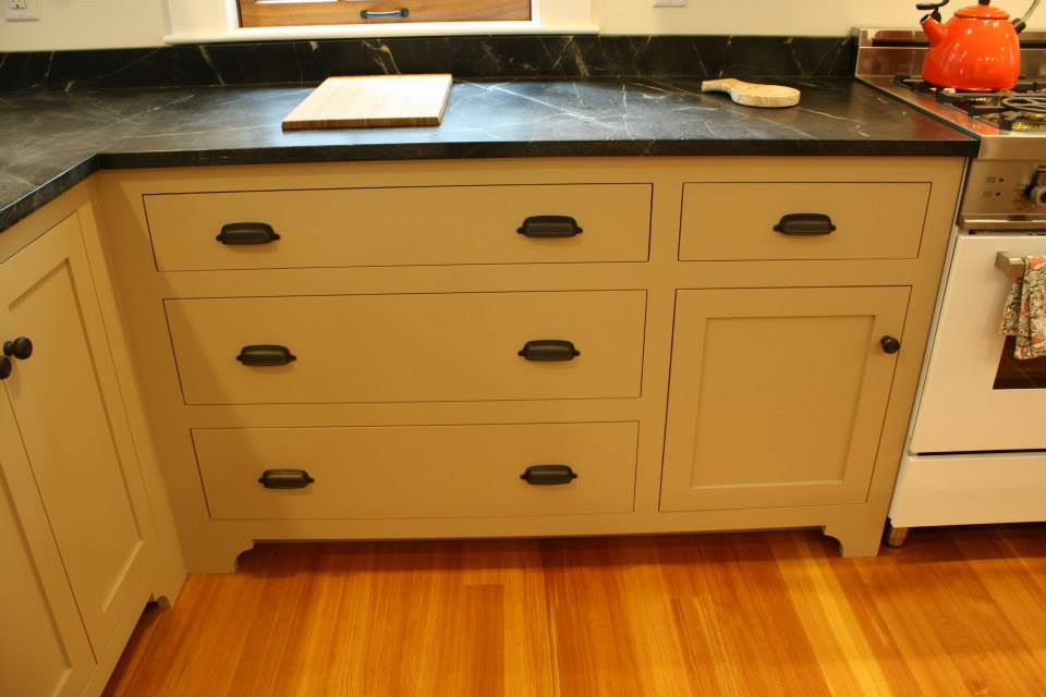 Kitchen cabinets with black countertop, drawers, and cabinet door, with hardwood floor.