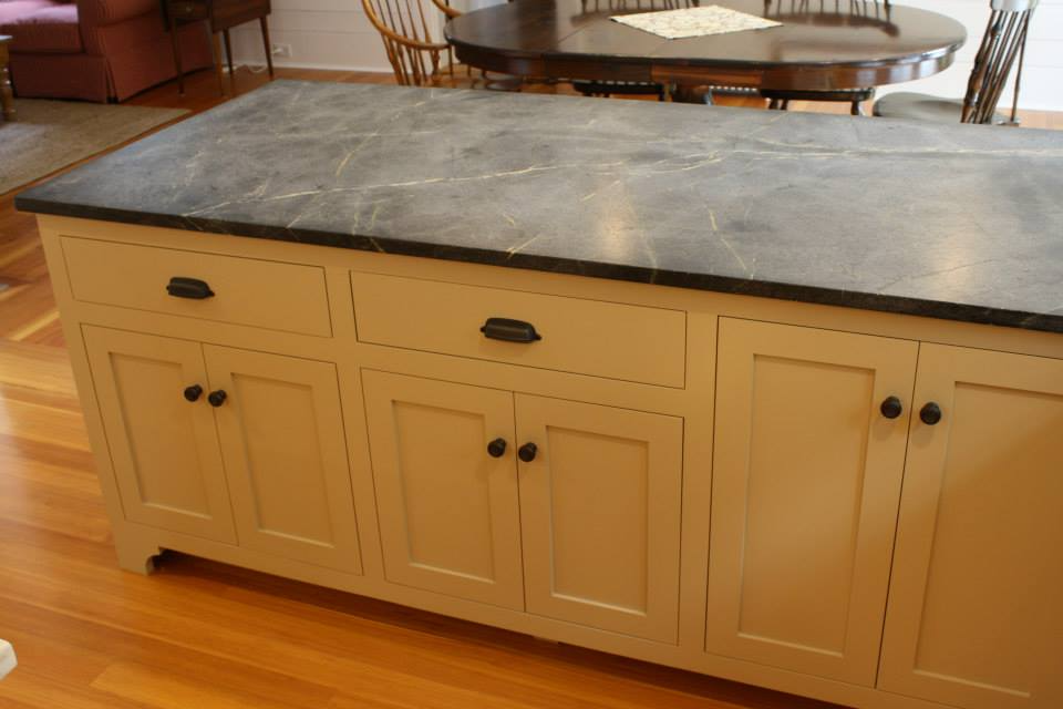 Kitchen island with beige cabinets, black countertop, and wood floors.