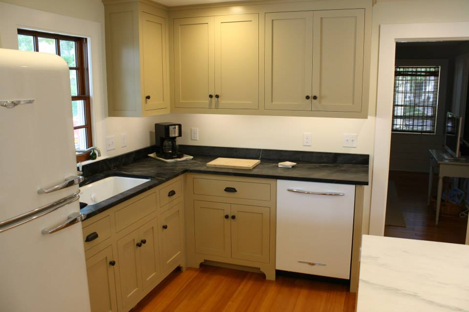 Kitchen with light green cabinets, black countertops, white appliances, and hardwood floors.