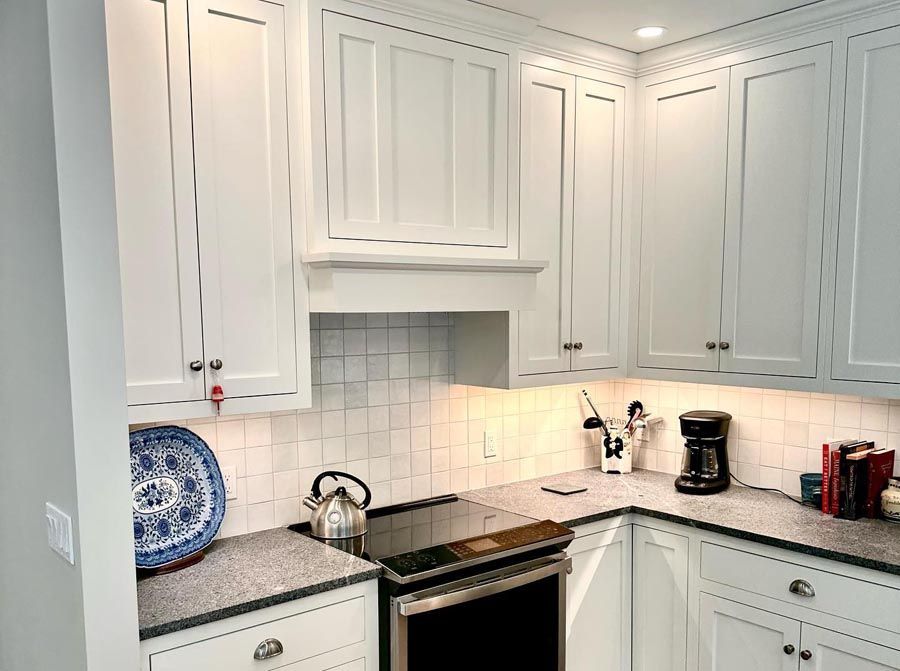 White kitchen cabinets with gray countertops, stainless steel stove, and white subway tile backsplash.