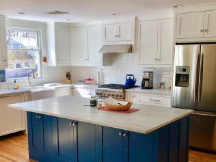 Kitchen with blue island, white cabinets, stainless steel appliances, and marble countertops.
