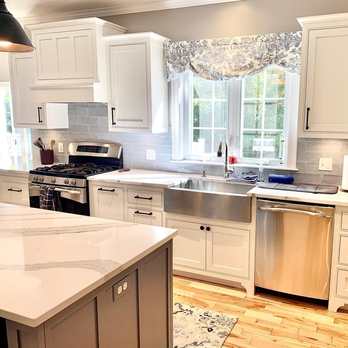 White kitchen with island, stainless steel appliances, and sink under window with patterned valance.
