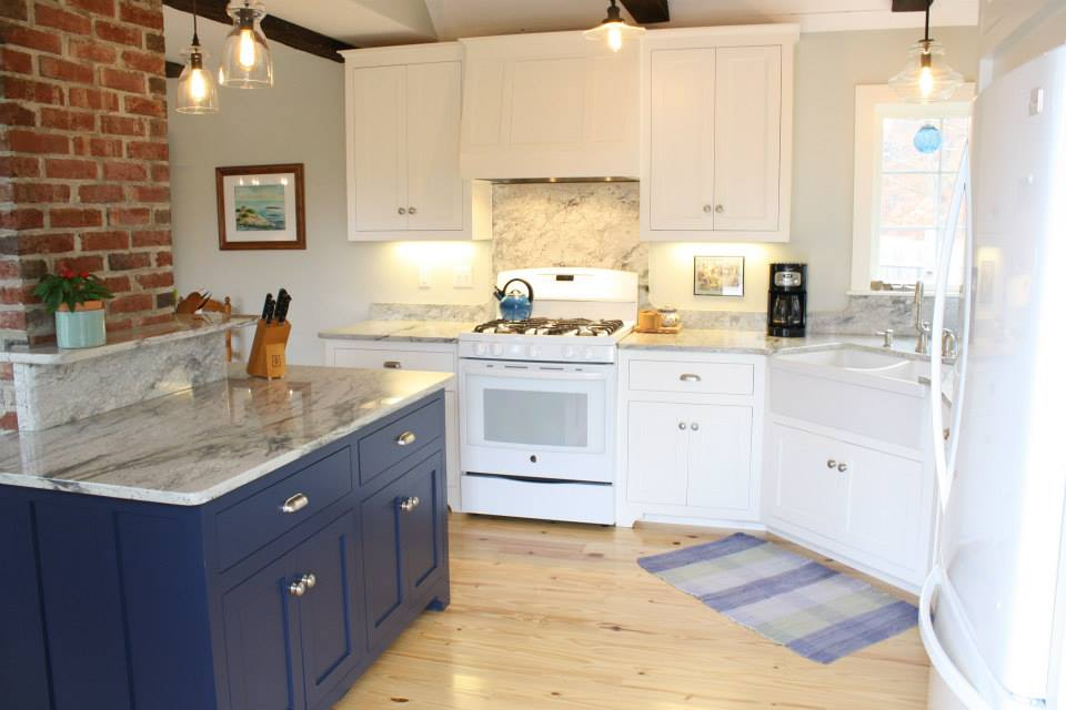 Kitchen with white cabinets, blue island, granite countertops, and brick wall.