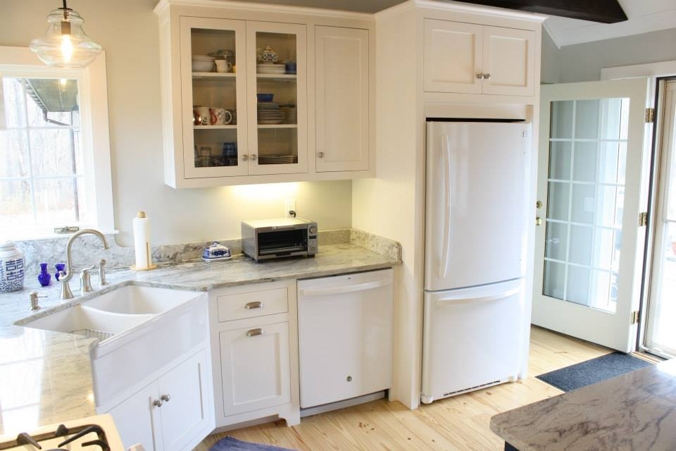 White kitchen with granite countertops, sink, cabinets, refrigerator, and glass door leading outside.