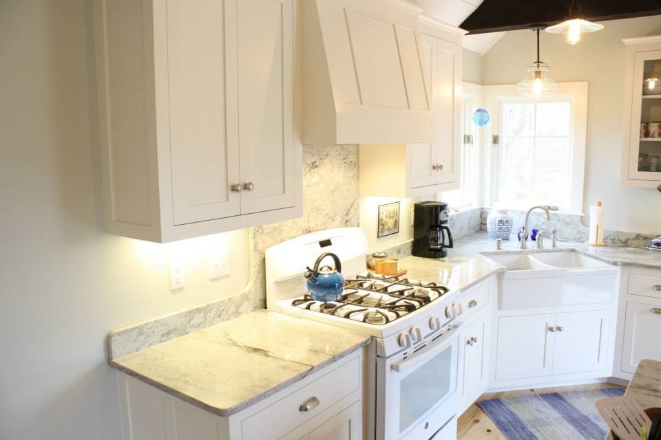 White kitchen with light-colored countertops, stove, sink, cabinets, and a window.