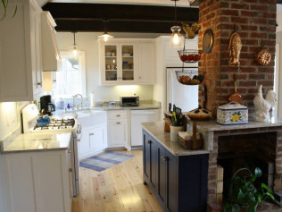 Kitchen with white cabinets, blue island, brick fireplace, and light wood floors.