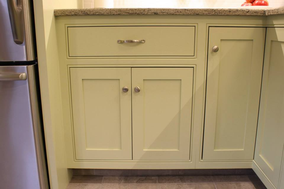 Light green kitchen cabinets with a drawer and doors, next to a stainless steel refrigerator.