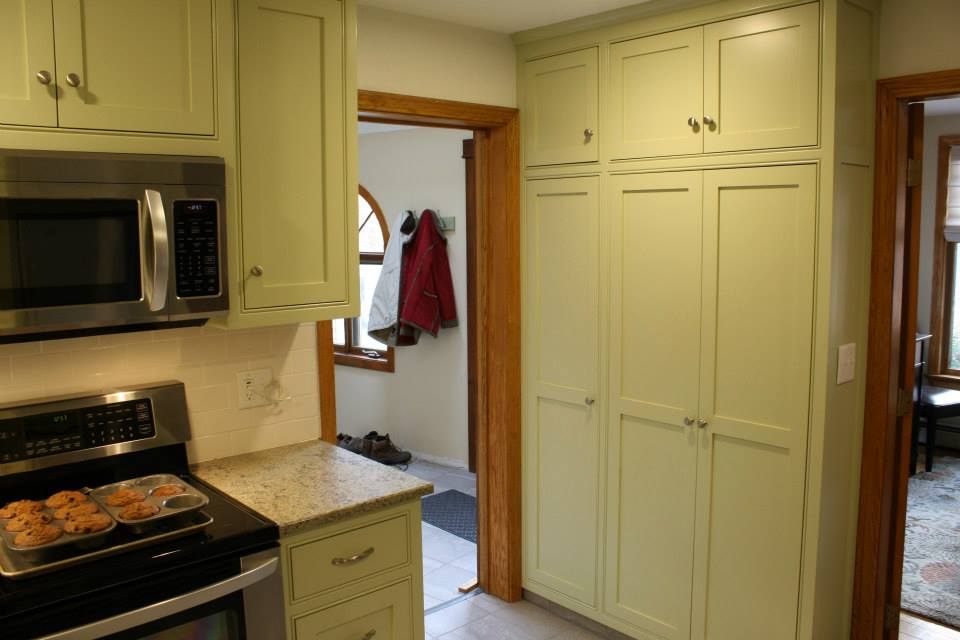 Kitchen with light green cabinets, a microwave, stove, and pantry. A doorway leads to another room.