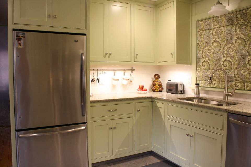 Kitchen with light green cabinets, stainless steel appliances, and patterned window covering.