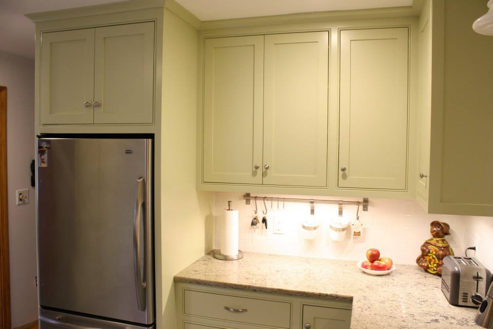 Kitchen with pale green cabinets, stainless steel refrigerator, and granite countertops.