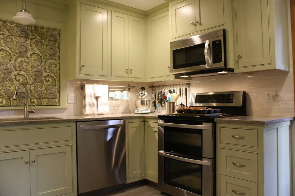 Green kitchen with stainless steel appliances, pale green cabinets, and patterned backsplash.