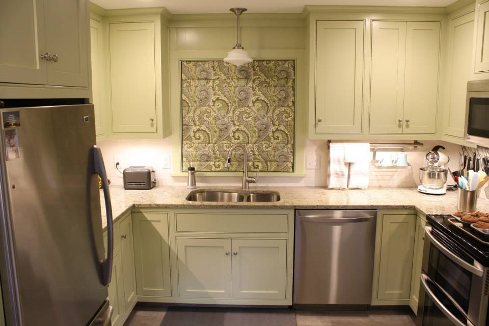 Kitchen with light green cabinets, stainless steel appliances, and a paisley-patterned window treatment.