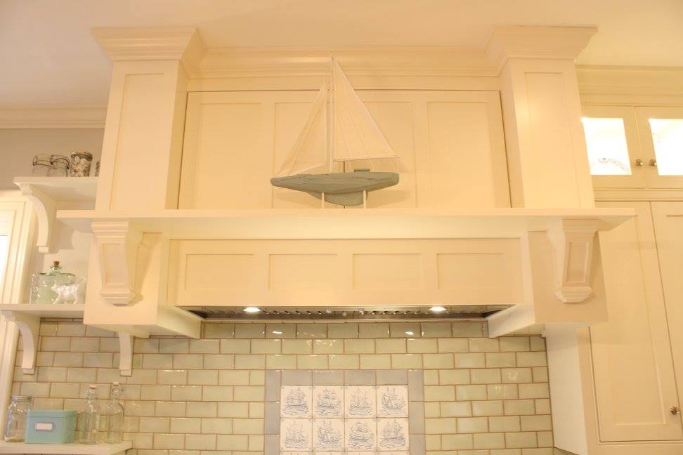 Cream-colored kitchen range hood with sailboat decor, above tiled backsplash and stove.