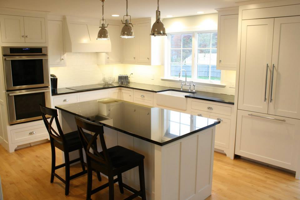 White kitchen with black countertops and island, stainless steel appliances, and wood floors.