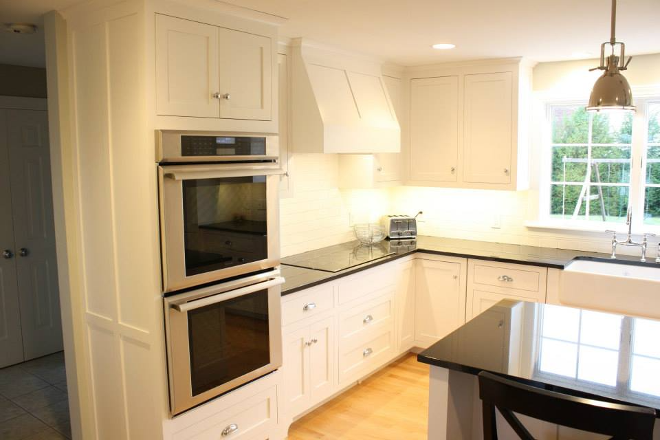 White kitchen with black countertops, built-in oven, and a window.