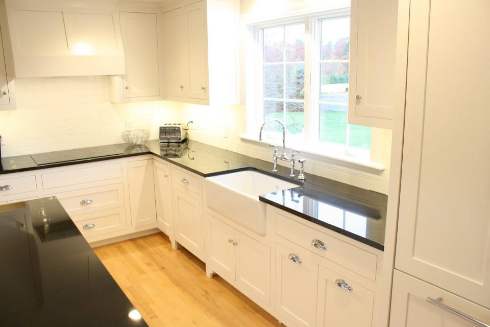 White kitchen with dark countertops, wood floor, and large window.