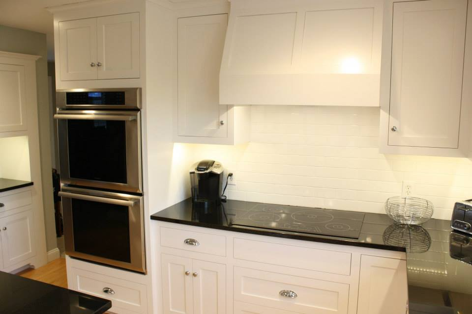 White kitchen cabinets and oven, black countertop, under-cabinet lighting.