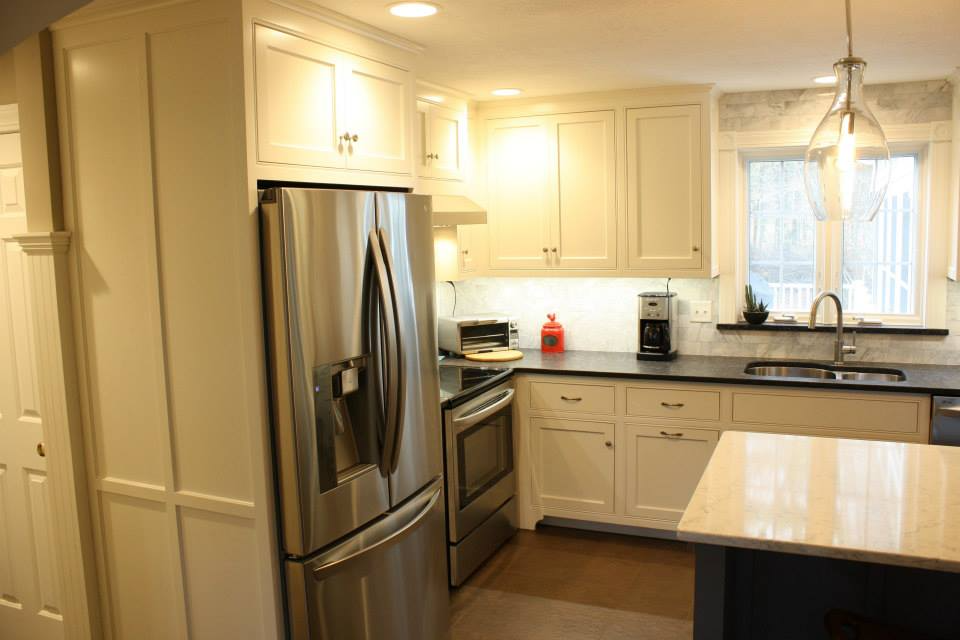 White kitchen with stainless steel appliances, dark countertops, and a window above the sink.