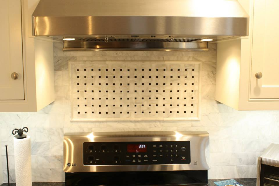 Stainless steel range hood above a stovetop, with a perforated tile backsplash.