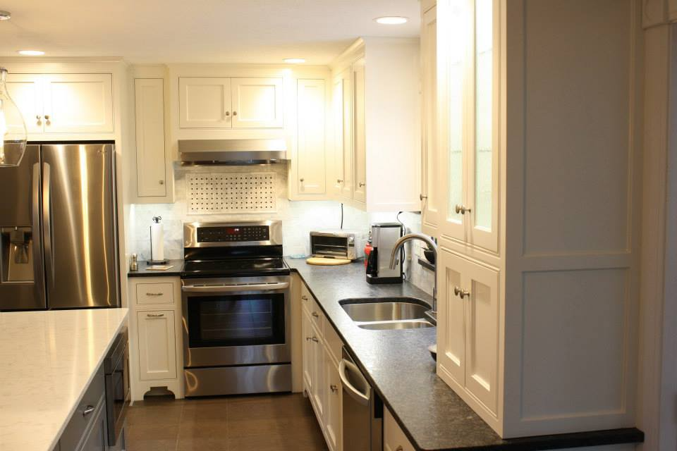 White kitchen with stainless steel appliances, dark countertops, and overhead cabinets.