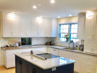 White kitchen with granite countertops, navy island, and recessed lighting.