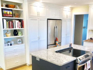 Kitchen with white cabinets, stainless steel refrigerator, and granite island with cooktop.