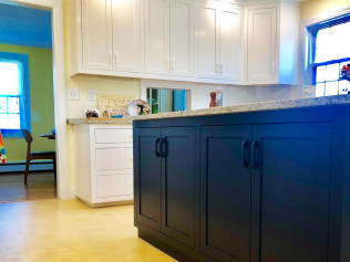 Kitchen with white upper cabinets, dark blue island, and granite countertops.