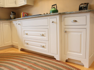 White kitchen cabinets with granite countertop, drawers and doors, and a striped rug.