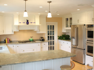 A well-lit white kitchen with stainless steel appliances, light-colored countertops, and an island.