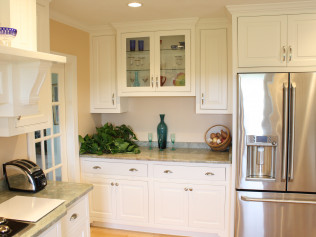 White kitchen cabinets with granite countertop, stainless steel refrigerator, and glass display cabinet.