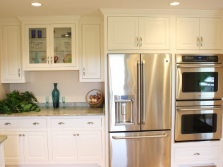 Cream-colored kitchen cabinets and stainless steel appliances; a refrigerator and double oven are featured.