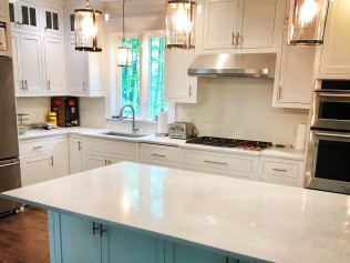 White kitchen with island, cabinets, appliances, and pendant lights.