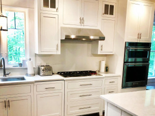 White kitchen with stainless steel appliances, cabinets, and a window.
