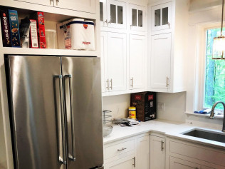 Stainless steel refrigerator next to white kitchen cabinets and countertop, with open shelves holding food items.