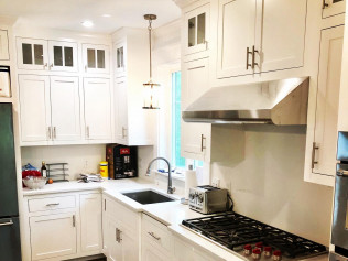 White kitchen with cabinets, stainless steel range hood, sink, and pendant light.