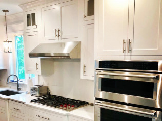 White kitchen with stainless steel appliances: oven, stove, vent hood, and cabinets.