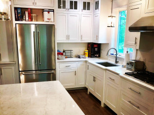 White kitchen with stainless steel appliances, white cabinets, and dark countertop with a sink.